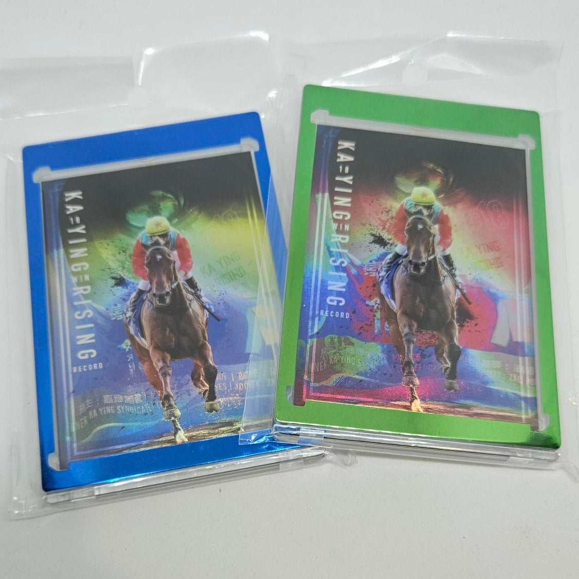 Two trading cards with colorful designs and text 'KA-YING RISING!' in a clear plastic sleeve on a white background.